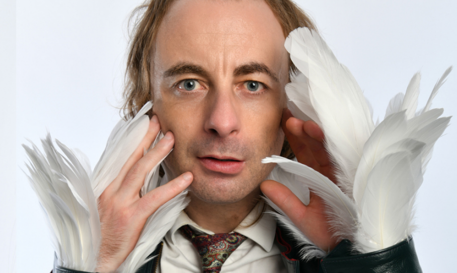 Paul Foot wears white feathered gloves and stares directly into the camera